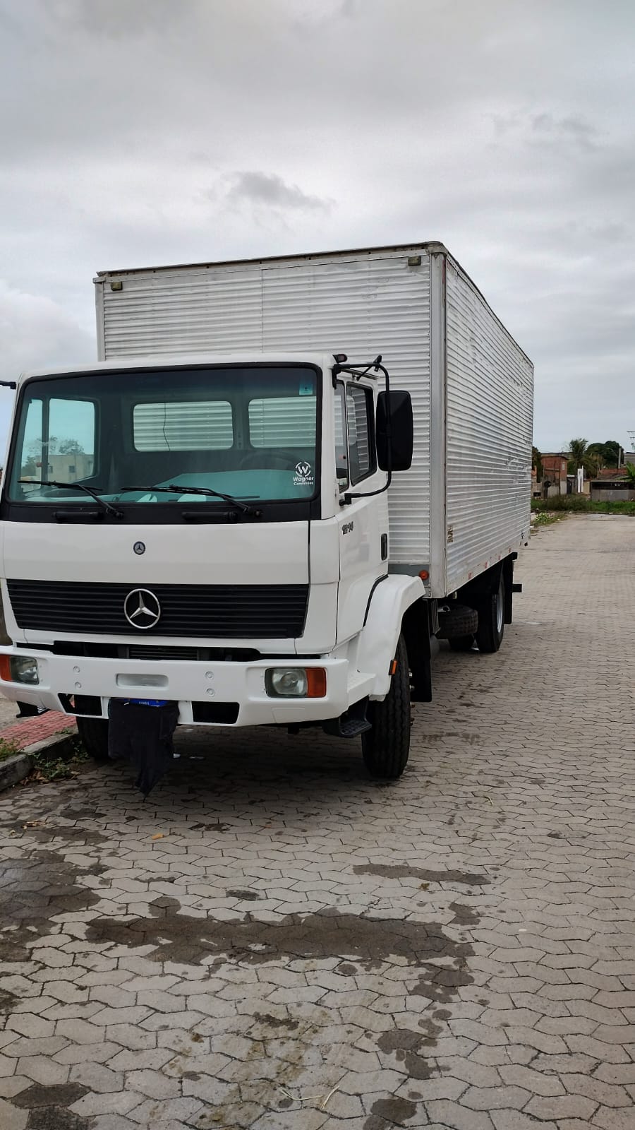 Mercedes 1214 branco com baú grande de alumínio estacionado em rua de bloquete